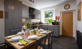 A modern kitchen with grey cabinets, a wooden dining table set for four, and a window providing a view of greenery outside.