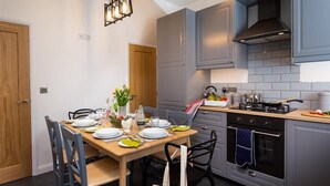Une cuisine moderne avec des meubles gris, une table à manger en bois pour quatre personnes et une cuisinière à gaz.