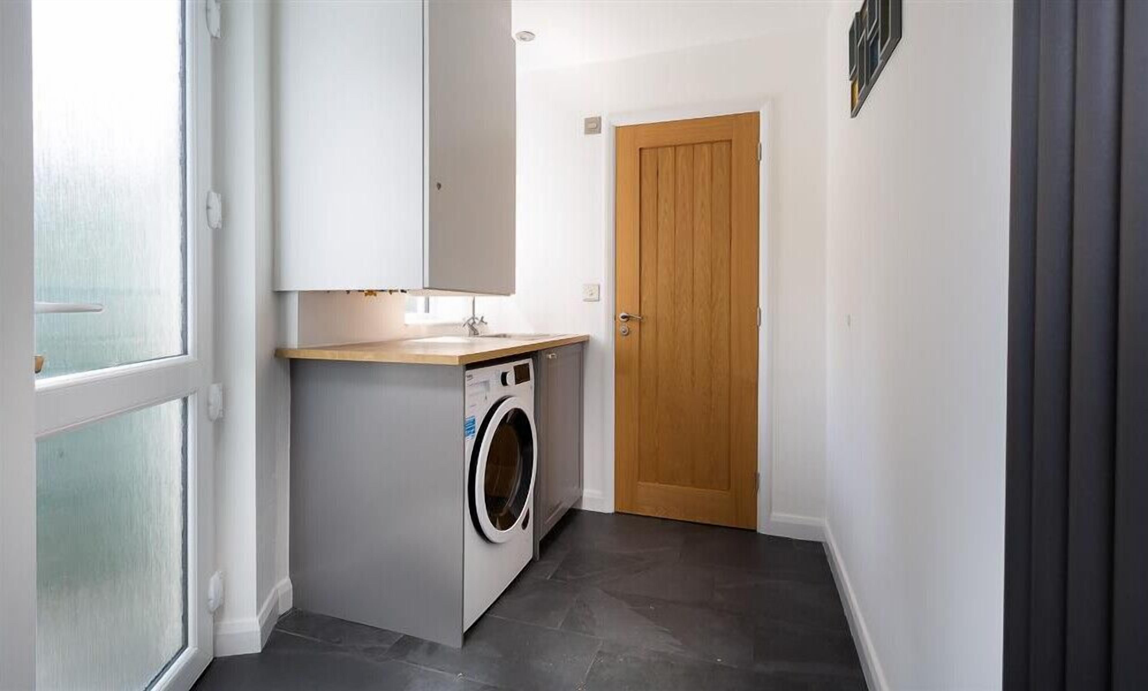 A laundry room with a washing machine, a sink, and a wooden door.