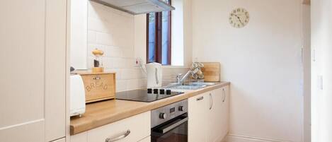 A compact kitchen with white cabinets, a wooden countertop, a built-in oven, and a window providing natural light.