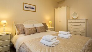 Un lit bien fait, avec des oreillers, une table de chevet avec une lampe, une commode avec des tiroirs et un tableau encadré accroché au mur.