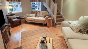 A cozy living room with a sofa, armchairs, a coffee table, and a staircase.