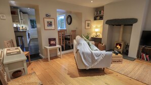 A cozy living room with a fireplace, a dining area with a table and chairs, and a kitchen in the background.