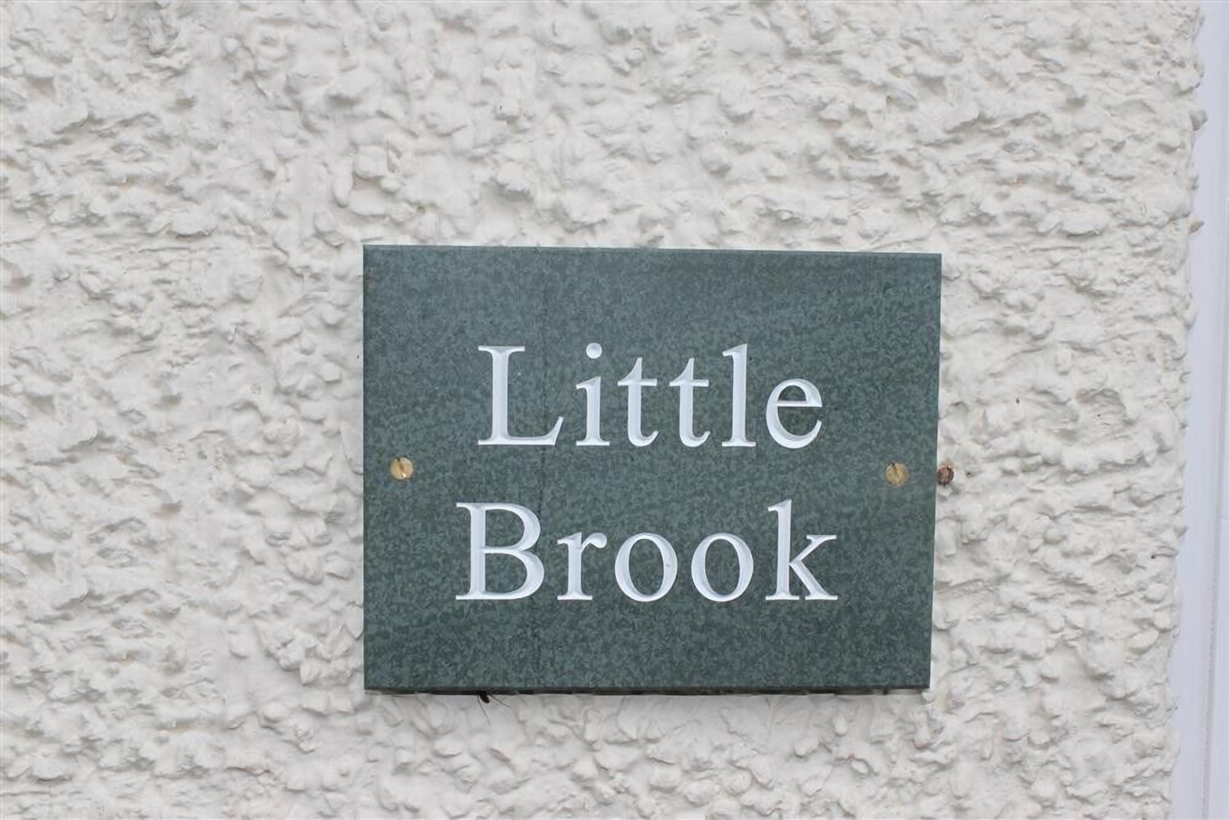Een bord met de tekst 'Little Brook' bevestigd aan een oppervlakte met structuur.