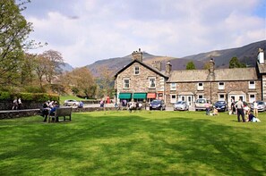 A stone building with a green awning, a grassy area, and parked cars. - The Gallery (Ambleside)