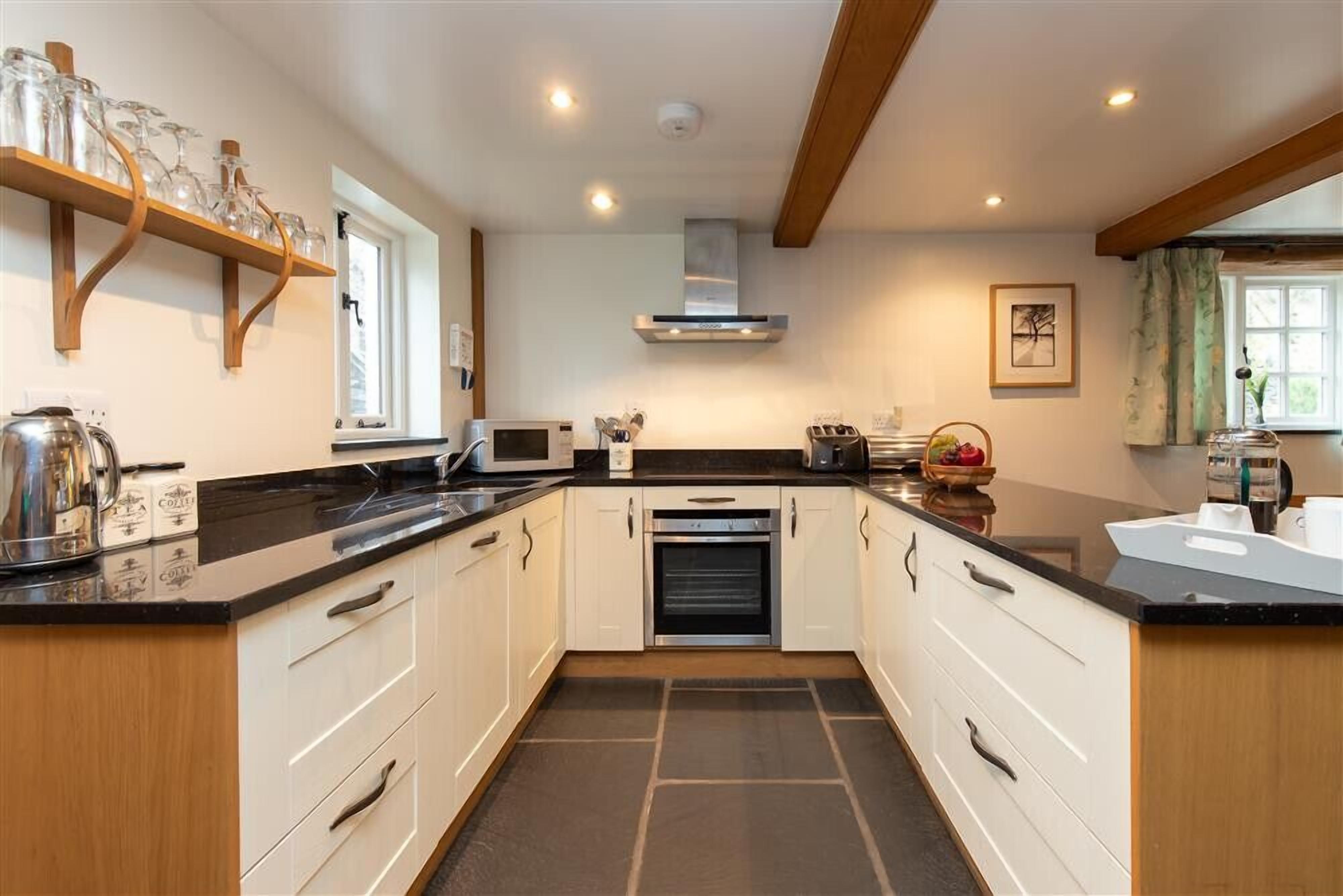 A modern kitchen with white cabinets, black countertops, and a built-in oven. There are shelves with glassware and a coffee machine on the counter.
