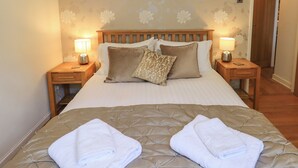 A neatly made bed with a quilted headboard, two bedside tables with lamps, and a floral-patterned wall.