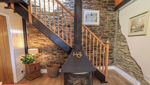 A cozy interior with a stone wall, a wooden staircase, a fireplace with a 'HO' symbol, and a framed picture on the wall.