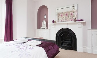 Quarto com cama, lareira e espelho na parede.