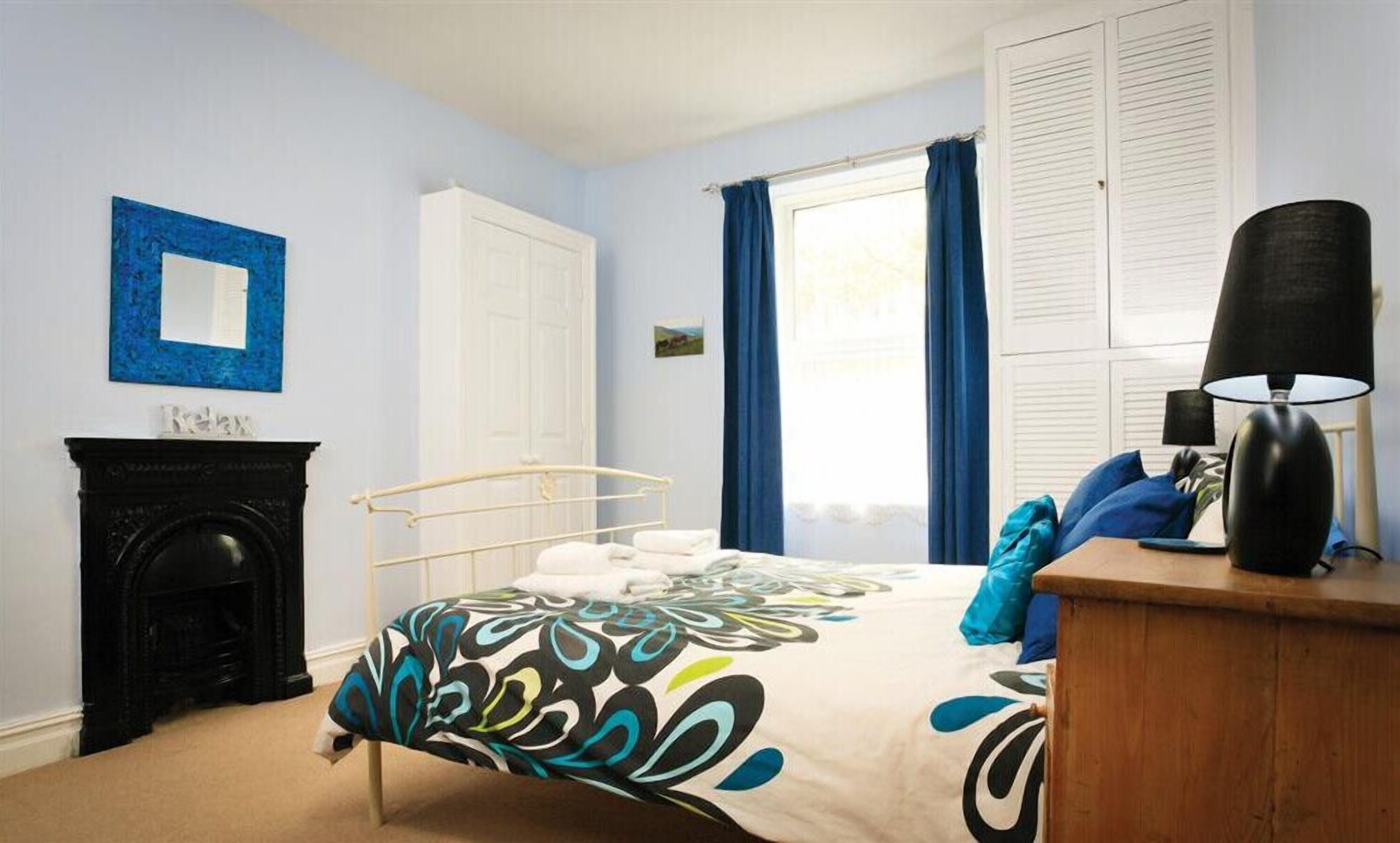A bedroom with a bed, a fireplace, a window with curtains, and a lamp.