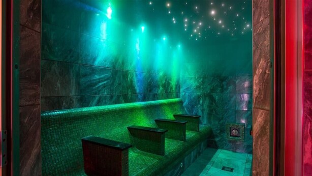 Una habitación tenuemente iluminada, con tonalidades verdes, una pared de piedra y un suelo de baldosas.