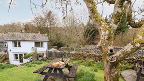 Une maison blanche avec un mur de pierre et une clôture en bois, dans un jardin où se trouve une table de pique-nique.
