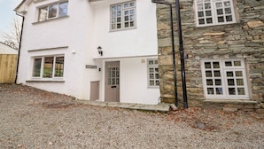 Une maison à deux étages, à l’extérieur blanc et agrémentée d’éléments en pierre, avec de nombreuses fenêtres et une porte bien visible.