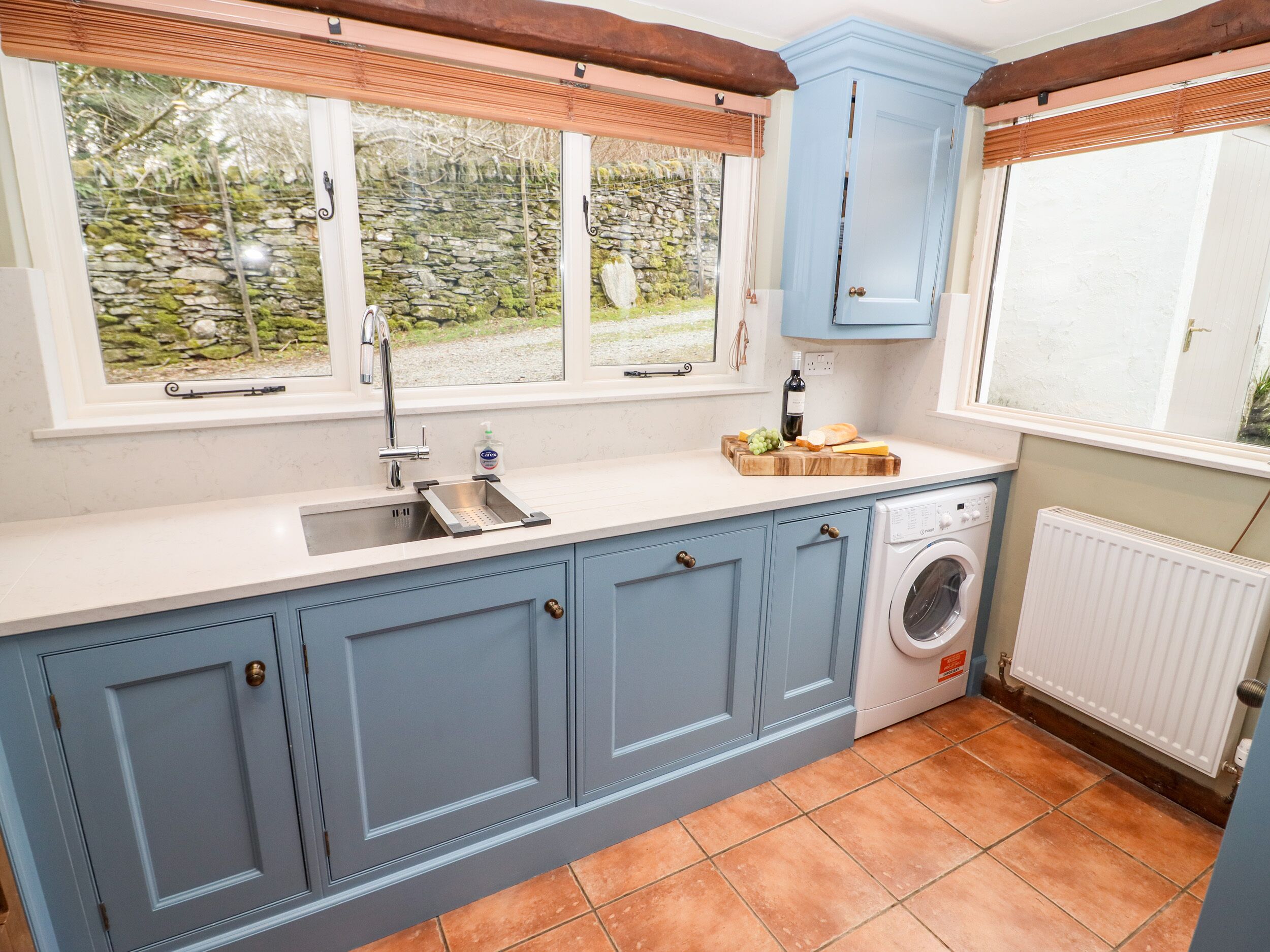 A compact kitchen with a built-in washing machine, a sink with a faucet, and a window overlooking a garden.