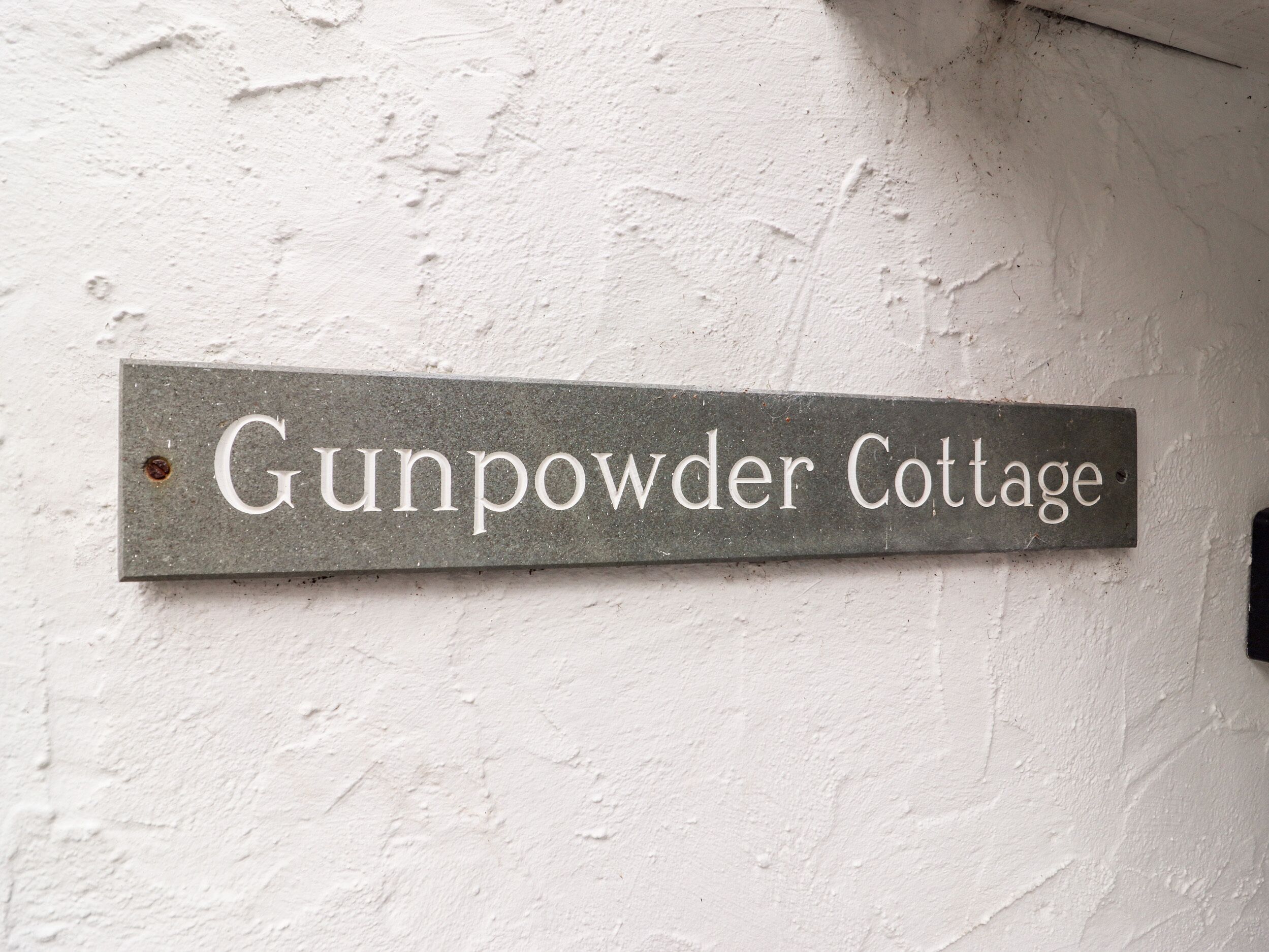 A metal sign with the text "Gunpowder Cottage" mounted on a white wall.