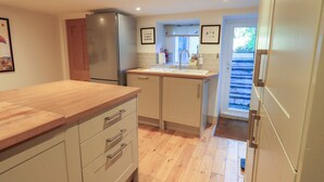 A modern kitchen with wooden countertops, stainless steel appliances, and a view of a staircase leading to another level. - Stones Throw Cottage (Ambleside)