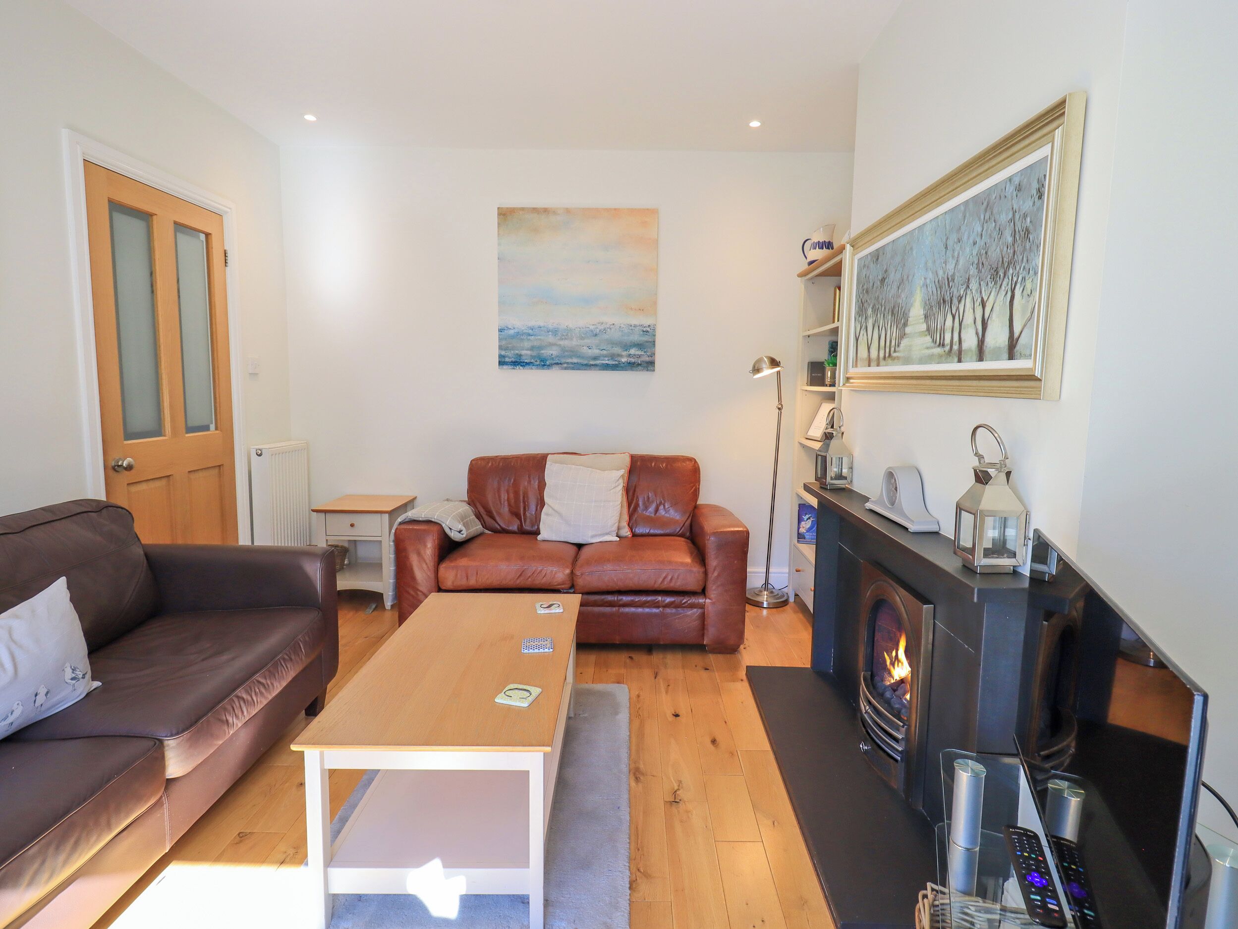 A living room with a brown leather sofa, a wooden coffee table, a fireplace, and a painting on the wall.