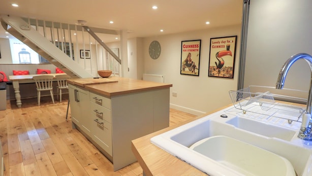 A modern kitchen with a wooden island, a built-in sink, and a staircase leading to a dining area. - Stones Throw Cottage (Ambleside)