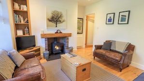 A cozy living room with a fireplace, leather sofas, a bookshelf, and a television. - Stones Throw Cottage (Ambleside)