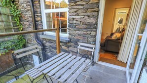 A balcony with a wooden table and chairs, stone walls, and a glass railing. - Stones Throw Cottage (Ambleside)