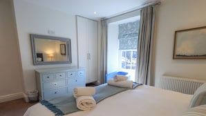 A bedroom with a bed, a dresser, a mirror, and a window with curtains. - Stones Throw Cottage (Ambleside)
