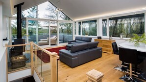 A modern living room with a fireplace, large windows, and a balcony. - Tall Trees (Windermere)