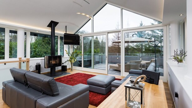 A modern living room with a fireplace, leather sofa, and a large glass door leading to an outdoor area. - Tall Trees (Windermere)