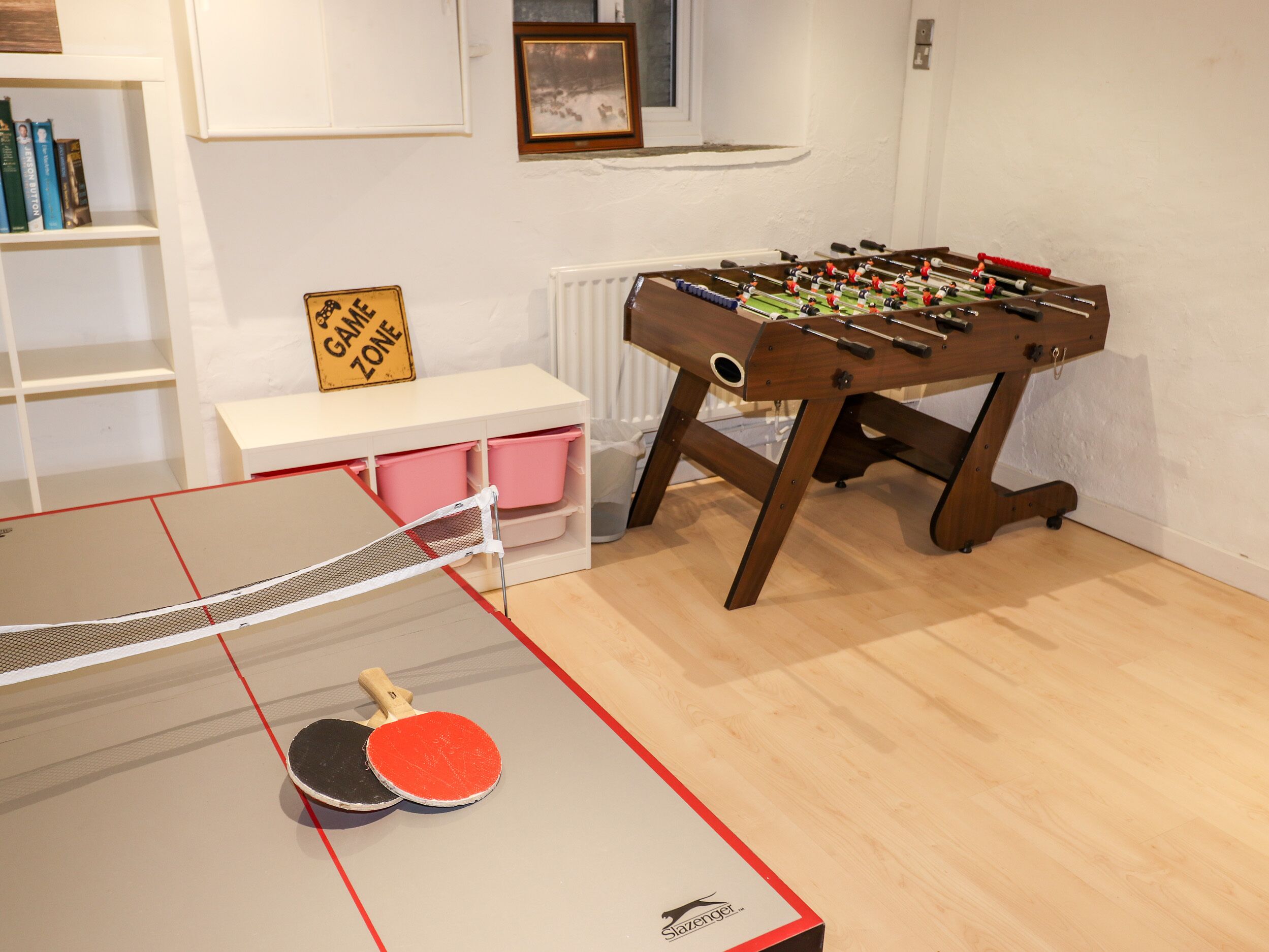 A ping pong table with two paddles, a foosball table, and a 'Game Zone' sign.