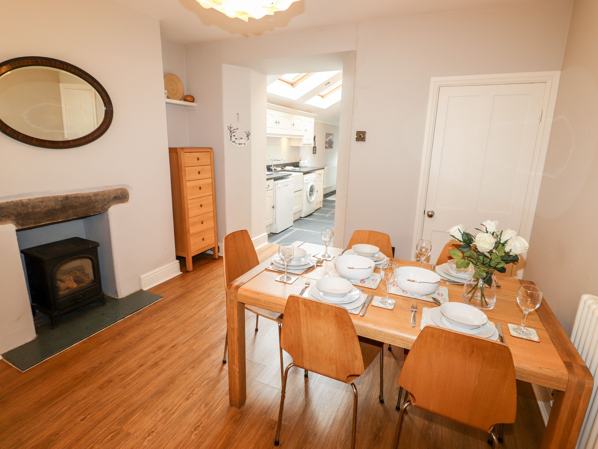 Comedor con una mesa de madera para cuatro personas, una chimenea y una cocina al fondo.