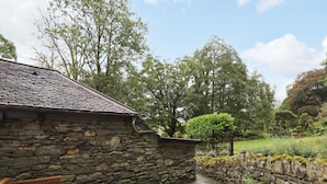 Un bâtiment en pierre avec un toit en tuiles, un mur en pierre et une terrasse pavée aménagée avec des meubles en osier.