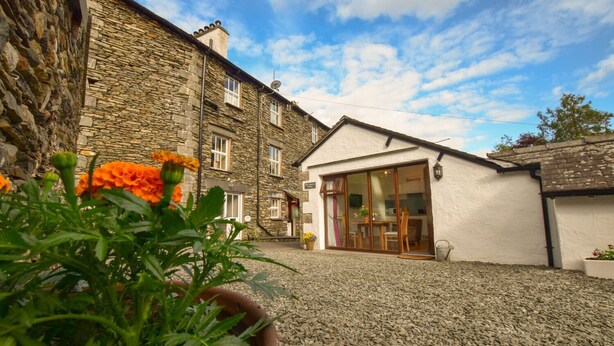 A stone building with a white extension featuring a glass door and a wooden table. - Old Sawrey Stores (Ambleside)