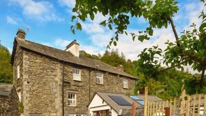 A stone building with a gravel driveway, a wooden fence, and a chair. - Old Sawrey Stores (Ambleside)