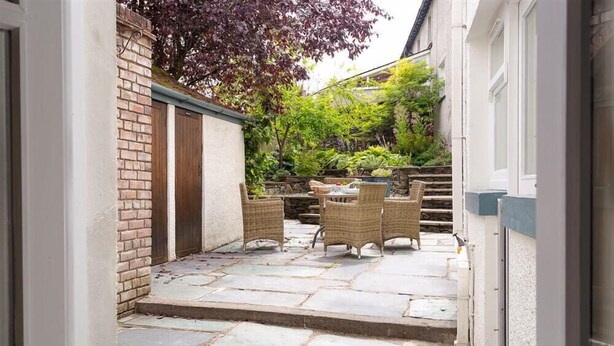 A stone patio with wicker furniture and a stone wall. - Pippin Cottage (Keswick)