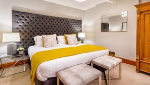 A bedroom with a tufted headboard, a large bed with a yellow throw, two bedside tables with lamps, a mirror, and a wooden wardrobe. - Pippin Cottage (Keswick)
