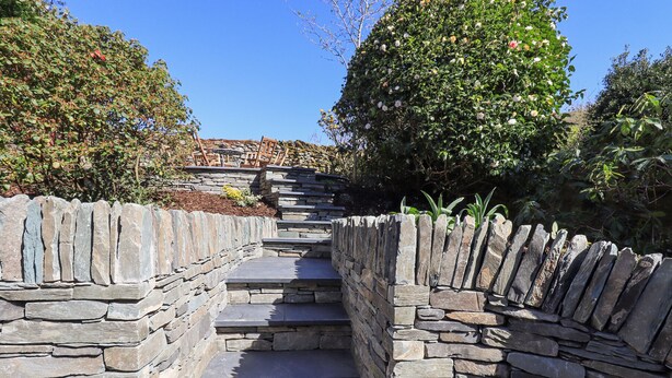 A stone staircase leading up to a stone wall with a garden on either side. - Striding Home (Ambleside)
