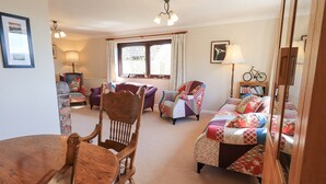 A cozy living room with a wooden dining table, two armchairs, a sofa, and a bookshelf. - Striding Home (Ambleside)