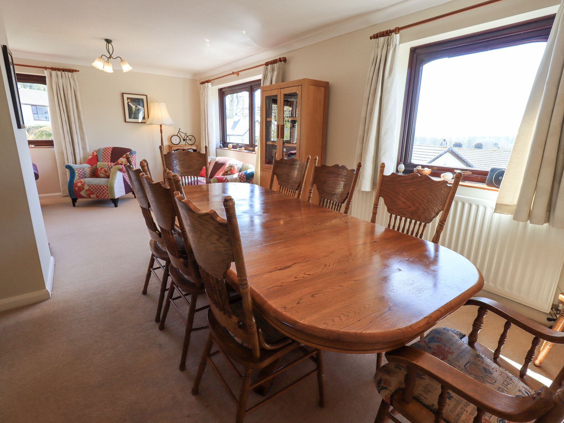 A dining room with a large wooden table surrounded by chairs, a bookshelf, and a view of a building through a window.