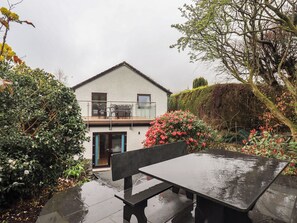 Ein zweistöckiges Haus mit Balkon, Terrassentisch und Bank.