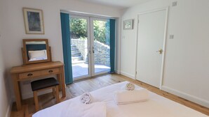 A hotel room with a bed, a desk with a chair, a mirror, and a door leading to a balcony. - Striding Home (Ambleside)