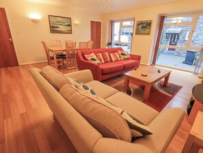 A living room with a beige sofa, a red sofa with patterned cushions, a wooden coffee table, and a dining area with wooden chairs and a table. - Molly's Cottage (Ambleside)