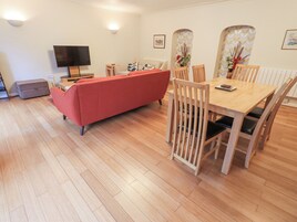 Una sala de estar moderna con un sofá rojo, una mesa de comedor de madera y sillas. Hay un televisor de pantalla plana y una mesita con una lámpara.