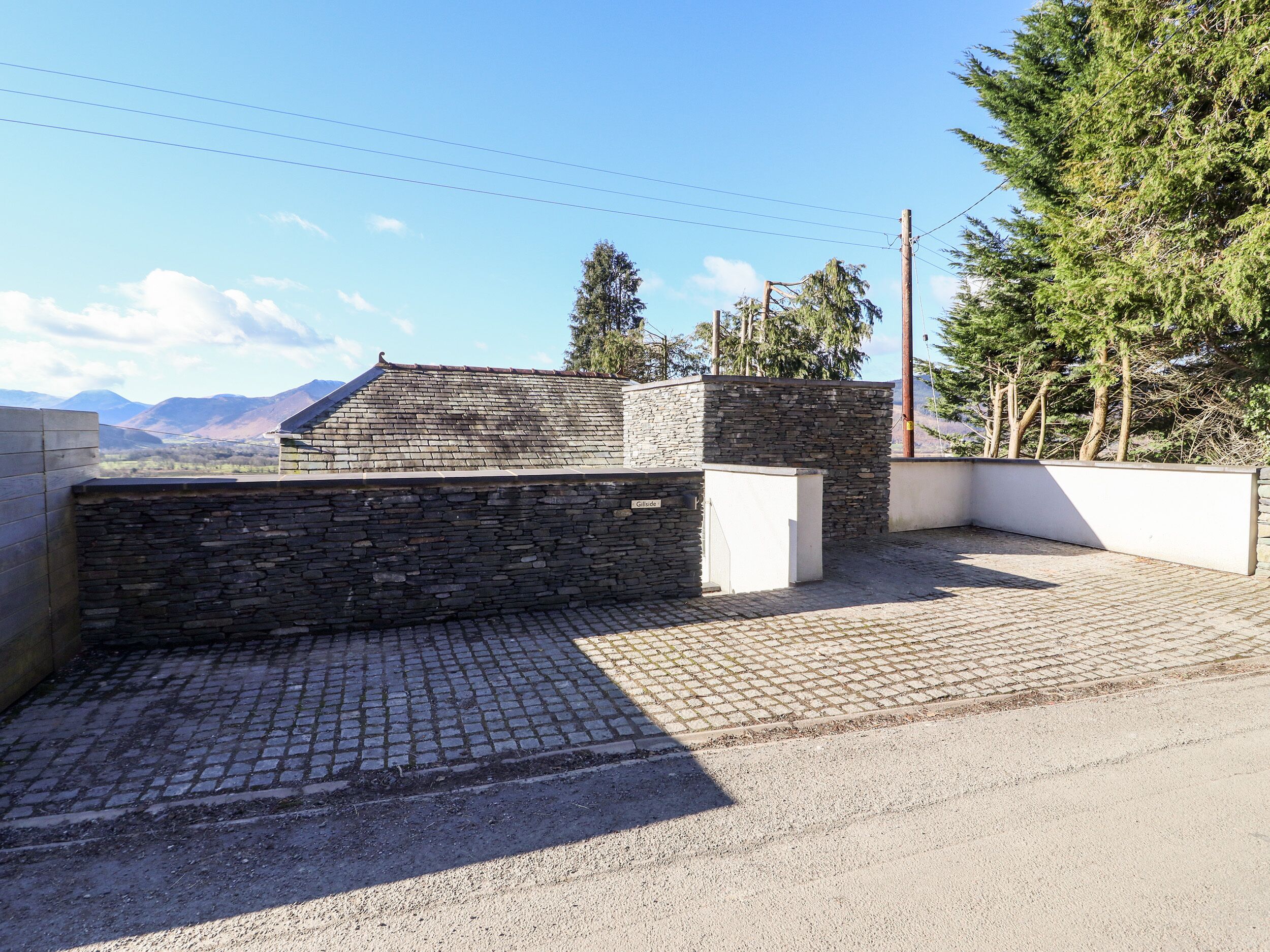 A stone building with a sloped roof, a paved driveway, and a view of mountains in the background.