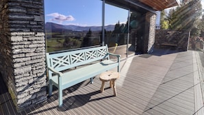 Una terraza de madera con un muro de piedra, un banco y una puerta de cristal que ofrece vistas a las montañas.