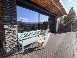 A wooden deck with a stone wall, a bench, and a glass door offering a view of mountains.