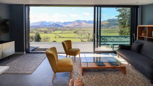 Una sala de estar moderna con un gran ventanal que da a un balcón, con vistas panorámicas a la montaña.
