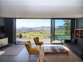 A modern living room with a large glass door leading to a balcony, offering a scenic mountain view.