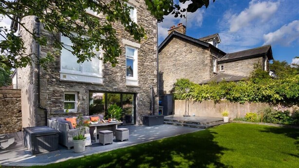 A stone house with a patio, outdoor seating, and a well-maintained lawn.