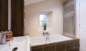 Un baño moderno con una bañera grande, una ventana con una planta y un espejo.