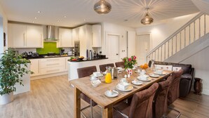 A modern kitchen with white cabinets, a wooden dining table set for breakfast, and a staircase leading to another level.