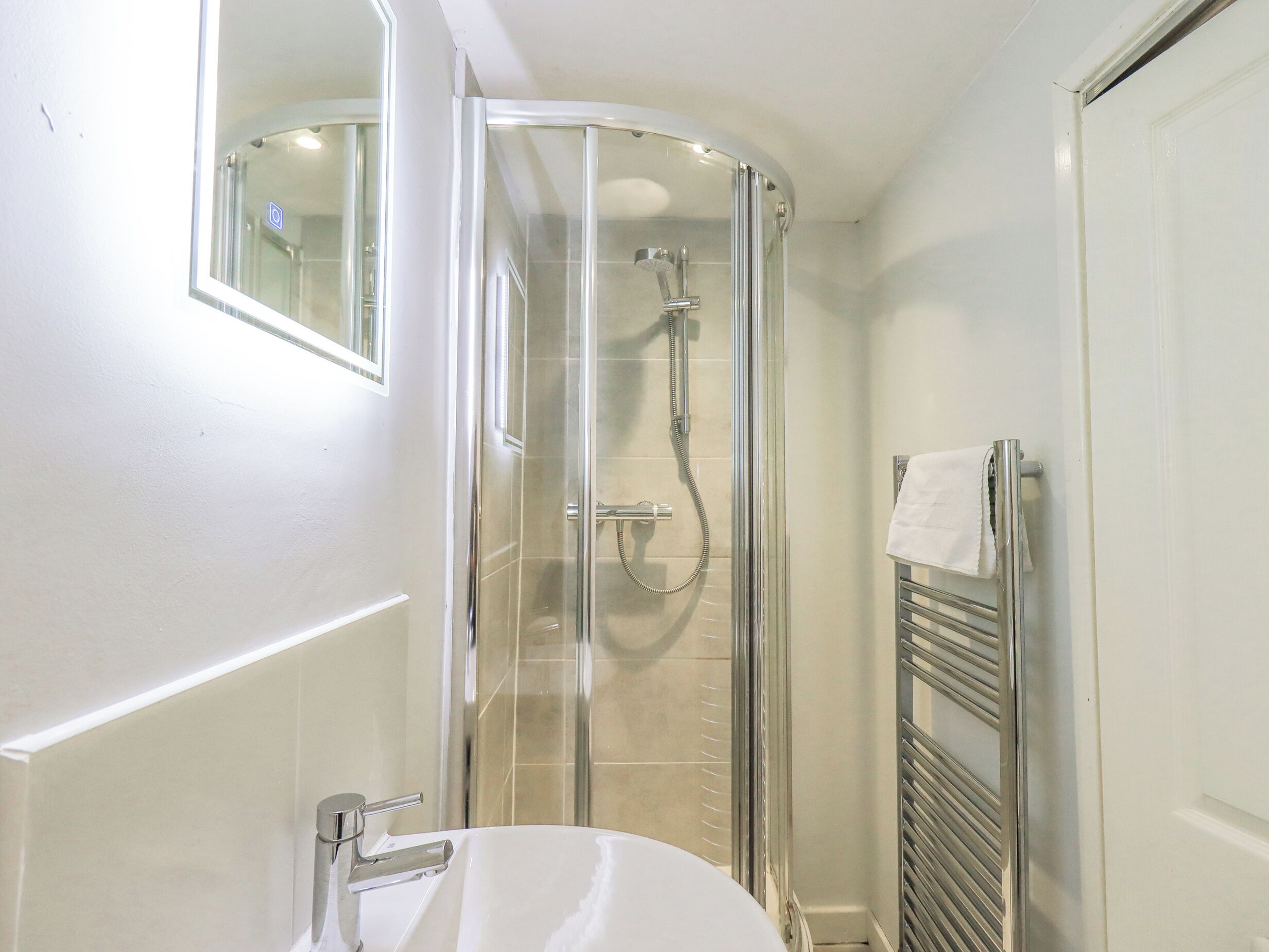 Un baño moderno con ducha de vidrio, lavamanos blanco y toallero.
